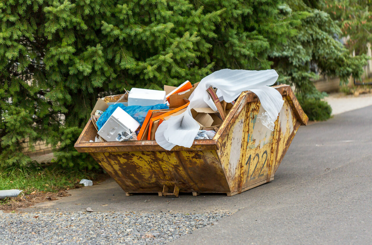 Overflowing rusty metal container or skip hire for construction waste with cardboard boxes and other plastic trash