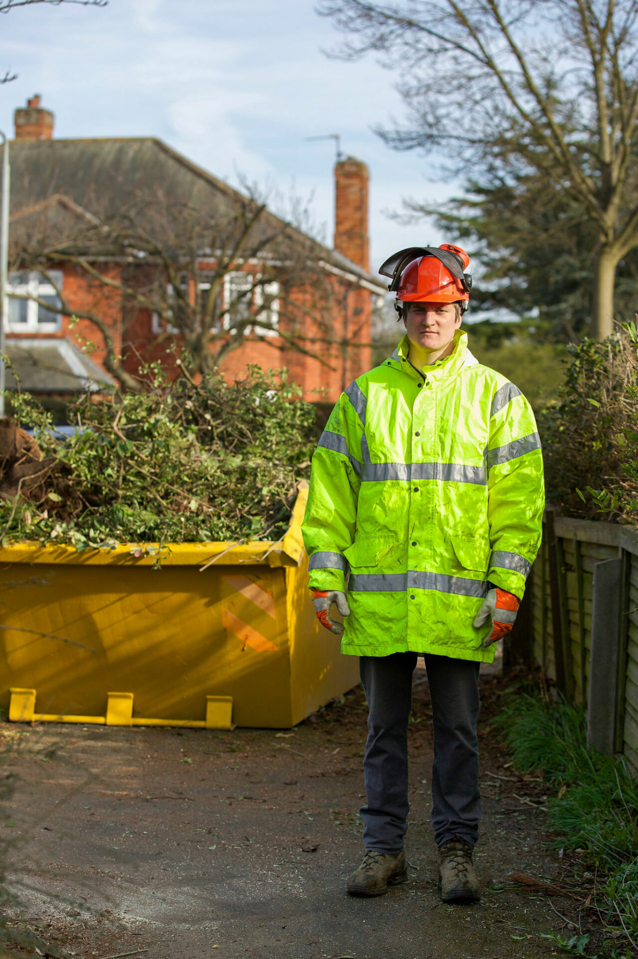 Tree surgeon standing in front of skip full of tree cuttings